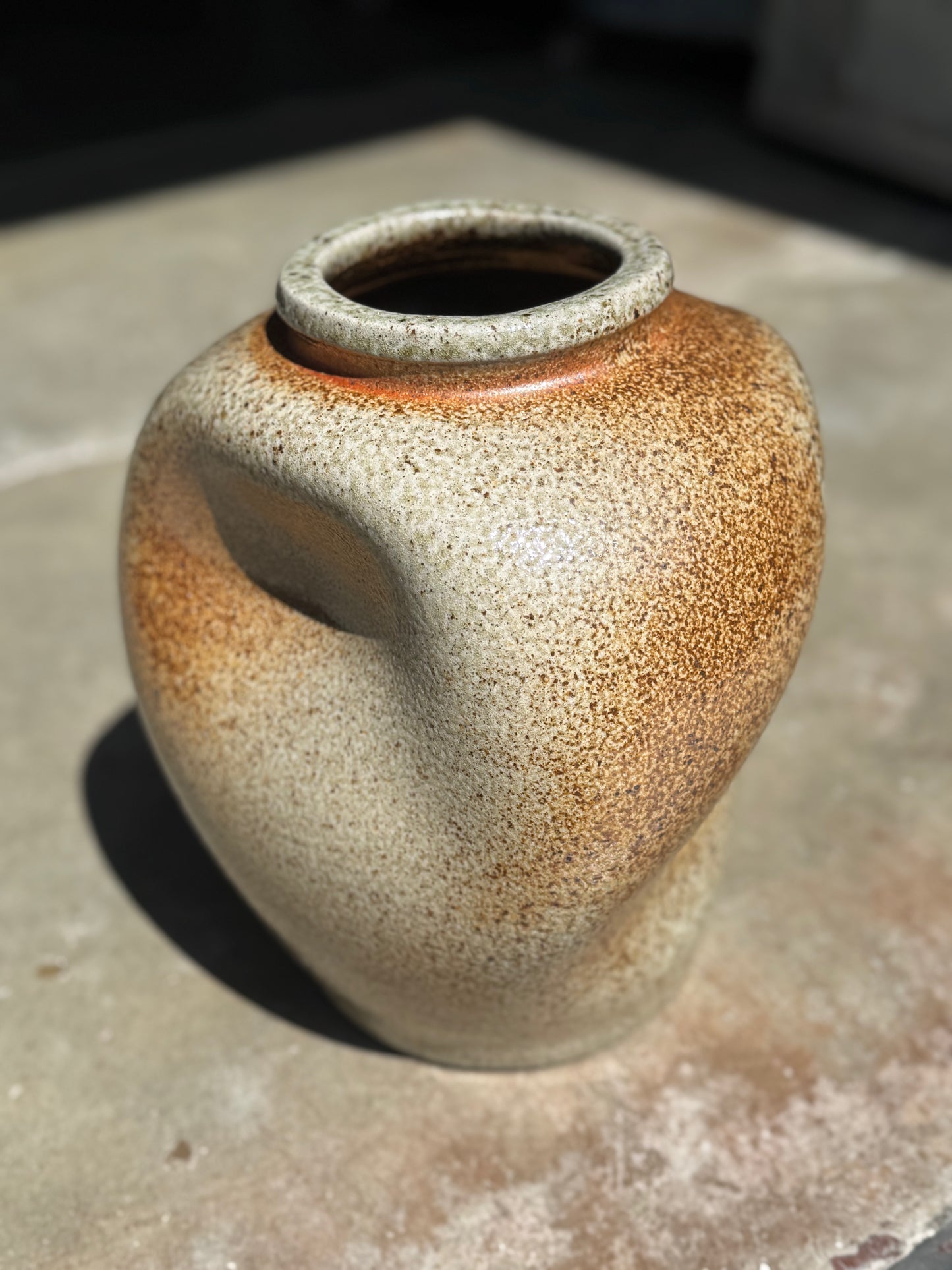 A hugged ceramic vase with a rounded body featuring a speckled glaze that transitions from warm beige to earthy brown.