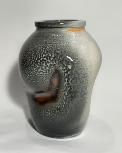 A hugged ceramic vase with a textured, speckled glaze transitioning from gray and white to a warm brown at the base, photographed on a neutral light gray background.