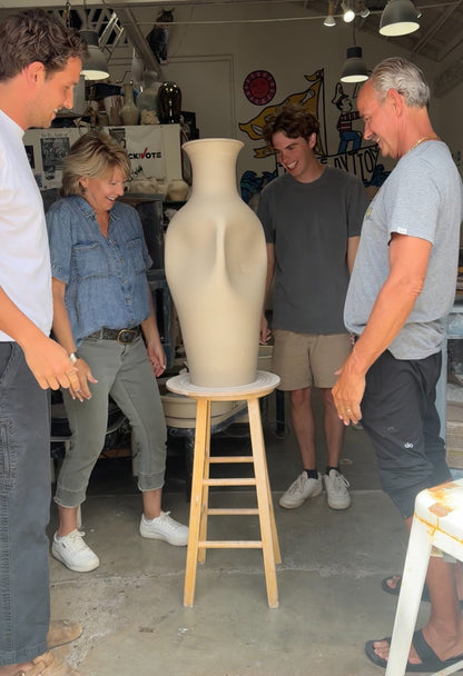A group of people gathered in a pottery studio around a large, hugged ceramic vase.